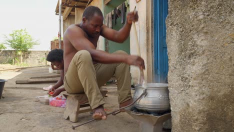 Man-stirs-banku-prepared-on-homemade-charcoal-stove,-Ghanaian-food