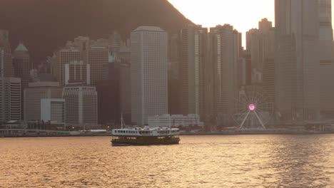 Ferry-Boat-Crossing-Victoria-Harbour-In-Hong-Kong-With-Cinematic-Golden-Hour-Sunlight-Overhead-And-Cityscape-In-Background
