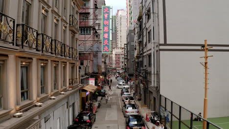 Hong-Kong-daytime-narrow-alley-with-neon-sign,-cars,-people,-basketball-court,-crowded-city,-busy-streets,-Tsim-Sha-Tsui,-pipes,-air-conditioners,-window,-close-up-shot,-overpopulation,-economic-hub