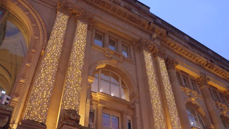 Low-Angle-Filmaufnahme-Eines-Architektonischen-Gebäudes,-Das-Zu-Weihnachten-Während-Des-Sonnenuntergangs-In-Manchester,-England,-Mit-Lichtern-Geschmückt-Ist