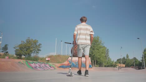 Kaukasischer-Mann-Geht-Auf-Beton-Skatepark-Boden-Mit-Stunt-Scooter-Daneben