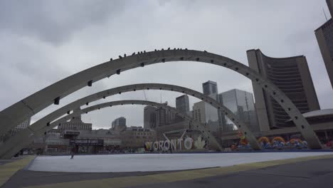 Wide-shot-of-people-ice-skating-at-Nathan-Phillips-Square-and-Toronto-City-Hall-in-Canada-during-cloudy-day