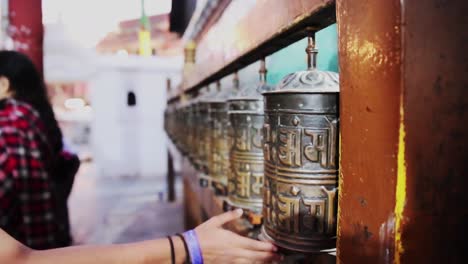 Tourists-walks-quickly-down-line-of-prayer-bells-outside-Nepalese-Buddhist-temple,-shallow-depth-of-field