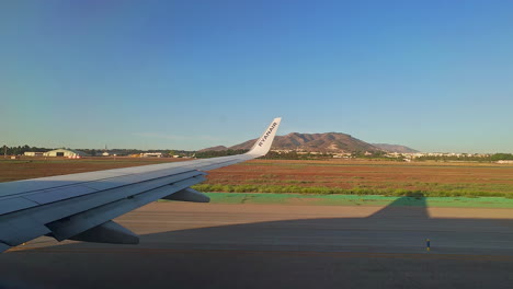 View-out-of-aeroplane-window-showing-wing-and-mountainous-landscape-surrounding-airport-runway