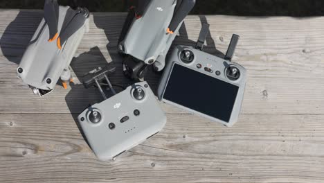 Overhead-View-of-Folded-DJI-Air-2S-And-Air-3-With-Controllers-On-Wooden-Bench