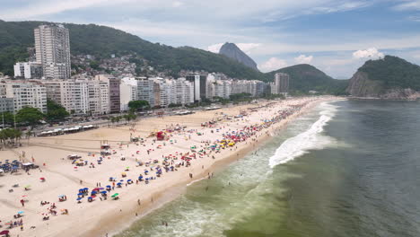 Drone-flight-along-iconic-Copacabana-stretch-of-white-beach-with-beachgoers,-Rio
