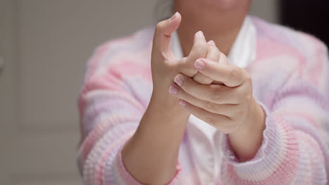 A-lady-wearing-a-pink-and-purple-stripes-sweater-is-pinching-her-hand-knuckles-and-fingers,-while-massaging-herself-to-relieve-them-of-inflammation-and-pain