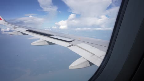 View-from-airplane-window-showing-wing-and-clouds,-with-clear-skies-and-earth-far-below