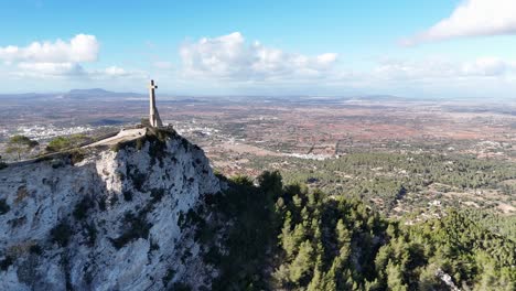 Aerial-approaching-shot-of-Sant-Salvador-Stone-Cross-on-hilltop-and-beautiful-scenic-landscape-of-Mallorca-Island,-Spain
