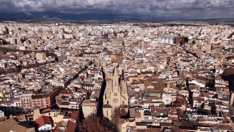 Aerial-Establishing-shot-of-historic-Basilica-de-Sant-Francesc-and-cityscape-of-Palma-de-Mallorca-lighting-by-sun,-Spain