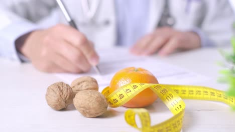 Close-up-shot-of-nutritionist-writing-a-Diet-prescription,-Walnuts,-tangerine-and-measuring-tape-on-table