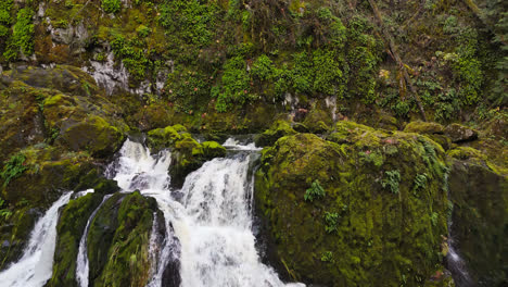 Atemberaubende-4K-Drohnenaufnahmen-Eines-Wasserfalls-Mit-Moosbedeckten-Felsen-Im-Wald