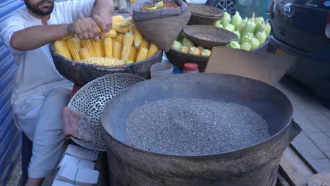 Closeup-parallax-shot-of-a-young-man-preparing-corns-for-roasting-during-evening-at-Saddar-Bazar-Street-of-Karachi,-Pakistan