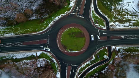 Aerial-speed-up-shot-above-traffic-at-a-snowy-roundabout,-cloudy-winter-day