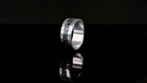 A-hand-crafted-ring-made-of-steel-and-epoxy-spinning-on-a-reflective-surface