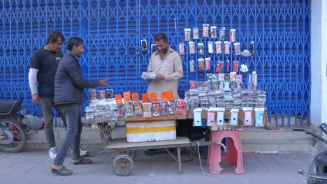 Cinematic-shot-of-a-hardworking-shopkeeper-selling-mobile-tempered-glass-at-a-roadside-stall-in-Saddar-Bazar-Street-of-Karachi-during-daytime-in-Pakistan