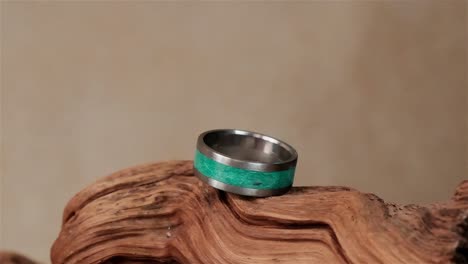 Ein-Handgefertigter-Ring-Aus-Edelstahl-Und-Einem-Grünen-Epoxidharzkern-Auf-Einem-Stück-Holz-Zur-Präsentation