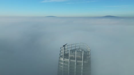 Aerial-footage:-Drone-tilts-up,-revealing-lone-skyscraper-breaking-through-thick-sunrise-clouds