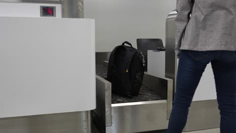Frau-Hebt-Ihren-Rucksack-An-Einer-Sicherheitskontrolle-Am-Flughafen-Mit-Digitaler-Gewichtsanzeige