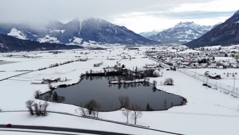 Aerial-establishing-shot-of-lake-surrounded-by-snowy-winter-landscape-and-swiss-alps-in-background