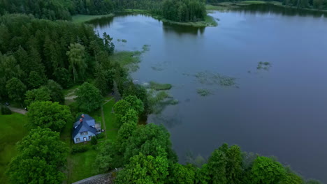 Aerial-view-overlooking-a-house-at-a-lake,-on-a-gloomy-summer-evening
