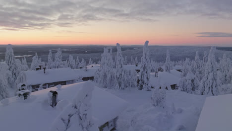 Aerial-view-of-cabins-and-snow-covered-trees-on-top-of-a-mountain-in-Lapland