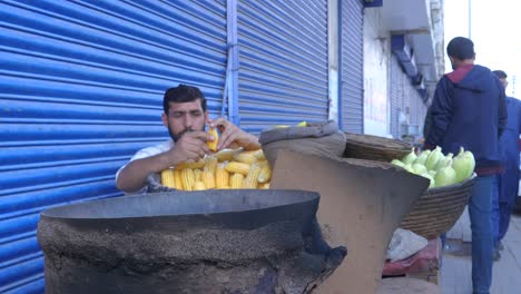 Slow-motion-shot-of-a-hardworking-man-stripping-corn-seeds-from-its-body-for-selling-during-daytime-in-Saddar-Bazar-Street-in-Karachi,-Pakistan