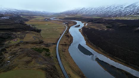 Aerial-circling-frozen-river-and-road-outside-Kirkjufell,-Iceland