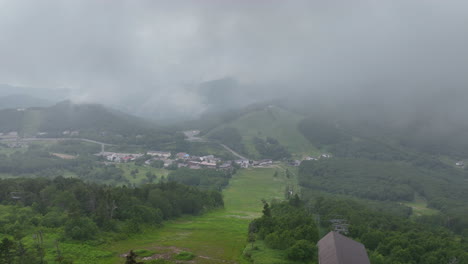 Aerial-overview-of-the-slopes-and-the-Shiga-Kogen-town,-foggy,-summer-day-in-Japan