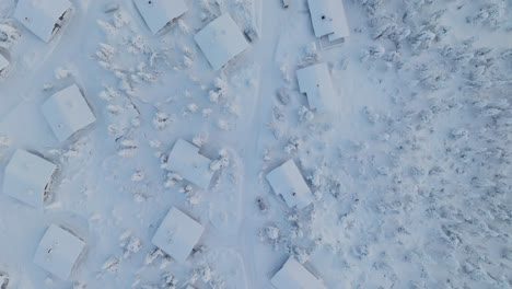 Top-down-drone-shot-over-snowy-cabins-on-top-of-a-fell,-polar-night-in-Lapland