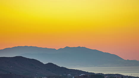 Golden-sunrise-over-mountainous-landscape-with-hazy-sky-and-silhouette-of-hills