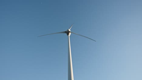 Wind-turbine-against-a-clear-blue-sky,-blades-in-motion,-harnessing-wind-energy