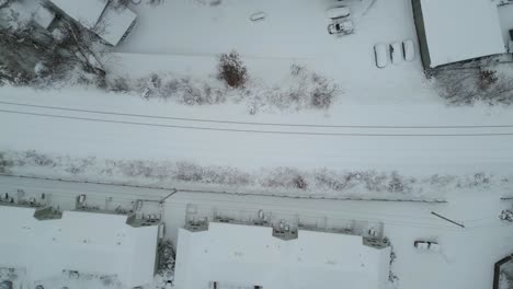 Aerial-satellite-zenithal-view-of-train-tracks-covered-in-snow-running-past-homes-and-businesses