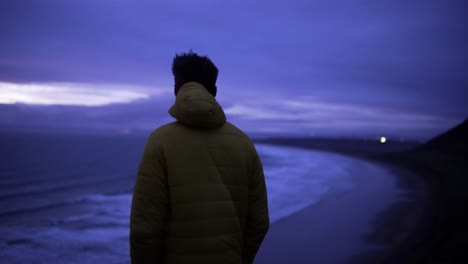 Man-overlooks-purple-sunset-on-windy-beach