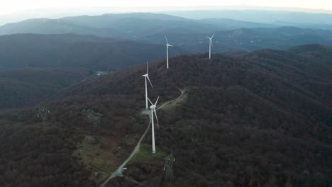 Wind-turbines-dominate-the-crest-of-forested-hills-in-a-fading-light,-an-aerial-view-of-sustainable-energy-in-the-wilderness
