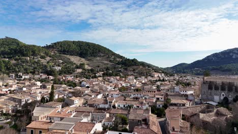 Ascending-drone-shot-showing-ancient-city-of-Esporles-with-green-mountains-in-background-in-summertime---Mallorca,-Spain
