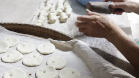 Chinese-cook-rolling-uncooked-dough-into-flat-round-and-piercing-a-hole-in-each-piece-using-traditional-wooden-rolling-pin-while-preparing-to-make-clay-oven-gilled-Chinese-flat-bread-or-"Huping"