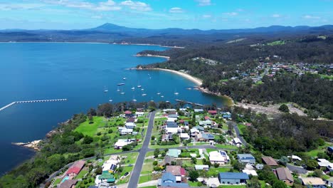 Drone-aerial-landscape-headland-coastline-bay-with-yachts-boats-housing-streets-roads-Cocora-beach-Eden-Sapphire-Coast-Australia-4K