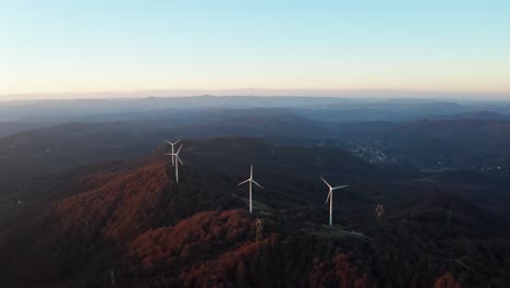 Ruhige-Luftaufnahme-Von-Windkraftanlagen-Auf-Bewaldeten-Hügeln-In-Der-Frühen-Dämmerung