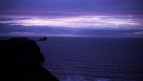 Purple-sunset-over-cliffs-and-a-small-island,-windy