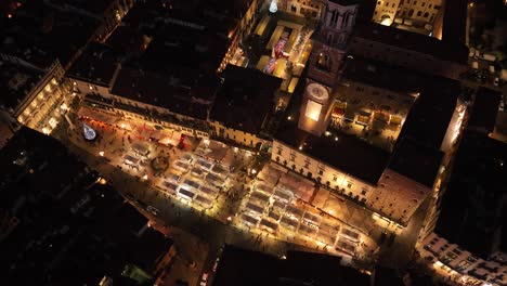 Aerial-Backward-Rotating-Clockwise-View-of-Erbe's-Square-illuminated-at-Night---Verona