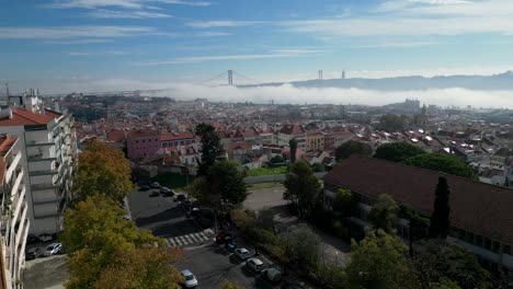 aerial-view-over-Lisbon-city-with-the-iconic-25-de-Abril-Bridge-emerging-majestically-from-a-misty-river,-creating-a-captivating-and-atmospheric-scene