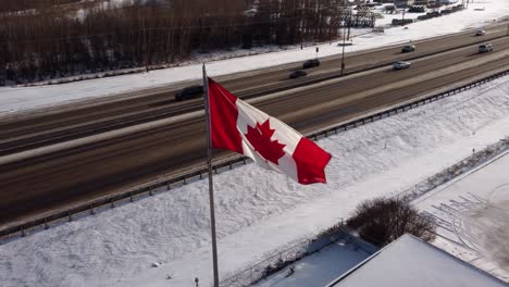 Winkende-Kanadische-Flagge-Mit-Einer-Autobahn-Im-Hintergrund-An-Einem-Sonnigen-Wintertag