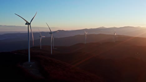 Early-morning-aerial-shot-of-wind-turbines-on-a-hilly-terrain-with-sunrise-casting-a-golden-light