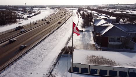 An-aerial-shot-of-a-curved-winter-highway-with-the-Canadian-flag-in-the-foreground
