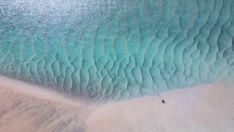 A-crystal-clear,-blue-lagoon-revealing-patterns-in-the-sand-caused-by-wave-formations