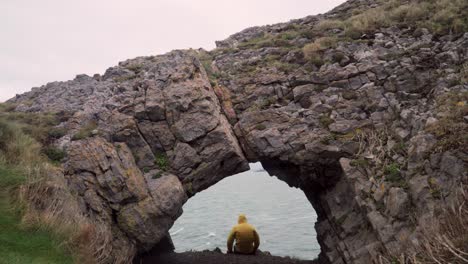 Mann-Blickt-In-Höhle-Aufs-Meer-–-Gelbe-Jacke