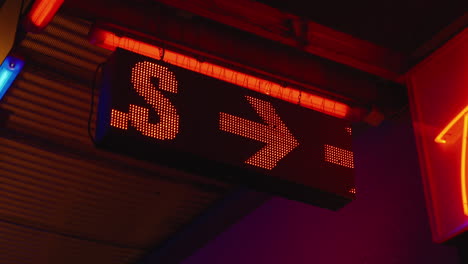 Red-LED-sign-displaying-the-word-girls-with-arrow-outside-strip-club,-close-up