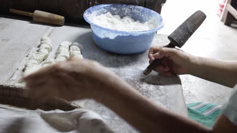 Food-vendor-rolling-uncooked-dough-into-flat-round-and-piercing-a-hole-in-each-piece-using-traditional-wooden-rolling-pin-while-preparing-to-make-clay-oven-gilled-Chinese-flat-bread-or-"Huping"