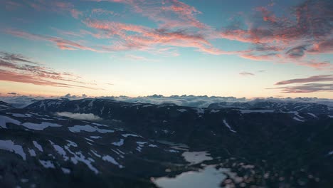 Flight-over-the-Strynefjellet-valley-with-pink-sunset-clouds-above-the-rocky-plateau-with-lakes-and-patches-of-snow